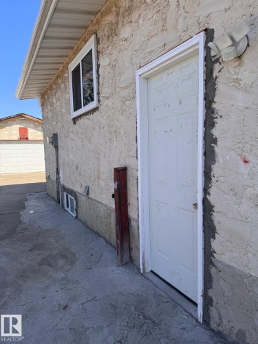 Stucco-finish exterior featuring a utility door with an exterior light fixture, a horizontal window, and concrete paving - 2910 132A Avenue, Edmonton, AB - Outdoor With Exterior