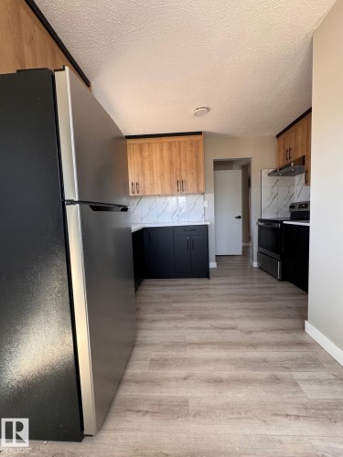 Modern kitchen featuring two-tone cabinetry, a stainless steel refrigerator, black range, and wood-finish flooring - 2910 132A Avenue, Edmonton, AB - Indoor Photo Showing Kitchen