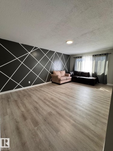 Spacious room featuring wood-finish flooring, a geometric accent wall, recessed lighting, and a large window with privacy coverings - 2910 132A Avenue, Edmonton, AB - Indoor Photo Showing Other Room