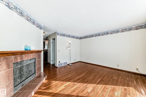 Unfurnished living room featuring hardwood / wood-style flooring, a tile fireplace, and a textured ceiling - 11922 138 Avenue, Edmonton, AB - Indoor Photo Showing Other Room