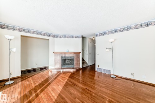 Unfurnished living room featuring hardwood / wood-style floors, a fireplace, and a textured ceiling - 11922 138 Avenue, Edmonton, AB - Indoor With Fireplace
