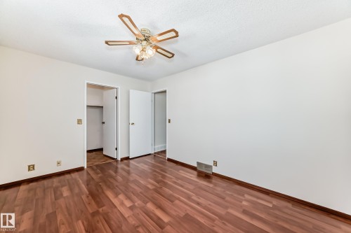 Unfurnished bedroom featuring dark wood-style flooring, ceiling fan, a spacious closet, and a textured ceiling - 11922 138 Avenue, Edmonton, AB - Indoor Photo Showing Other Room
