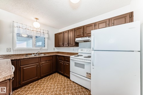 Kitchen featuring white appliances, pendant lighting, a textured ceiling, light floors, and dark wood finish cabinetry - 11922 138 Avenue, Edmonton, AB - Indoor Photo Showing Kitchen With Double Sink