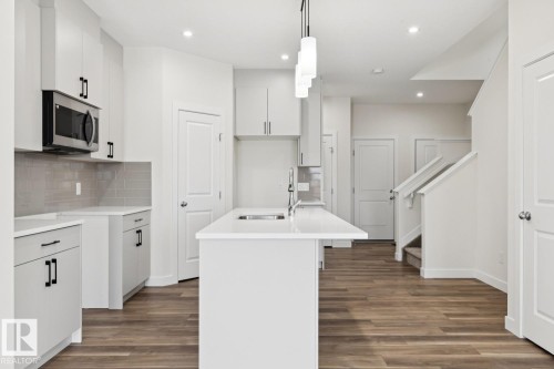 Kitchen with a center island with sink, stainless steel microwave, decorative light fixtures, and dark wood-style floors - 407 26 Street, Edmonton, AB - Indoor Photo Showing Kitchen