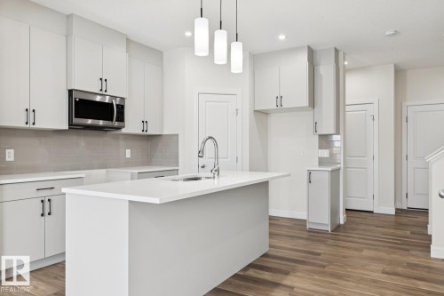 Kitchen with stainless steel microwave, hanging light fixtures, dark wood-type flooring, tasteful backsplash, and white cabinetry - 407 26 Street, Edmonton, AB - Indoor Photo Showing Kitchen With Upgraded Kitchen
