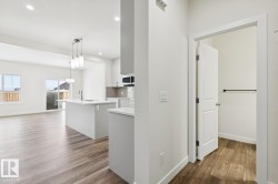 Kitchen featuring backsplash, dark wood-style floors, decorative light fixtures, a center island with sink, and white cabinetry - 
