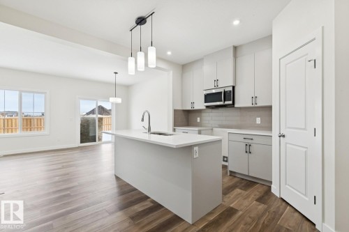 Kitchen with white cabinets, decorative backsplash, decorative light fixtures, stainless steel microwave, and dark wood-type flooring - 407 26 Street, Edmonton, AB - Indoor Photo Showing Kitchen