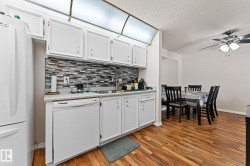 Kitchen with white cabinets, white appliances, a ceiling fan, light wood-style flooring, and backsplash - 