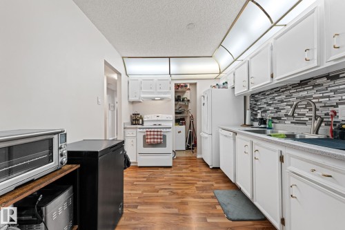 Kitchen featuring white cabinetry, light wood finished floors, white appliances, light countertops, and a textured ceiling - 36 2204 118 Street, Edmonton, AB - Indoor Photo Showing Kitchen