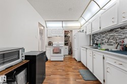 Kitchen featuring white cabinetry, light wood finished floors, white appliances, light countertops, and a textured ceiling - 