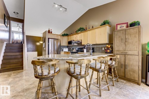 Kitchen with light wood finish cabinetry, light stone countertops, stainless steel appliances, a peninsula, and lofted ceiling - 20148 46 Avenue, Edmonton, AB - Indoor