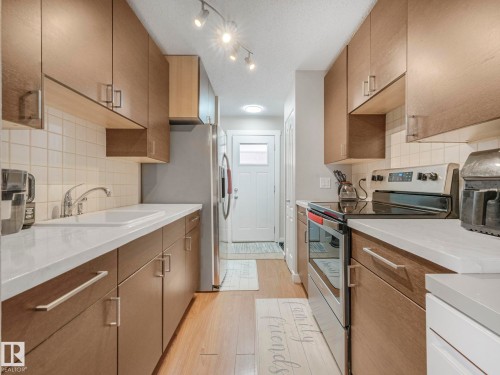 Kitchen featuring stainless steel appliances, light wood finished floors, a textured ceiling, backsplash, and light stone countertops - 13271 47 Street, Edmonton, AB - Indoor Photo Showing Kitchen