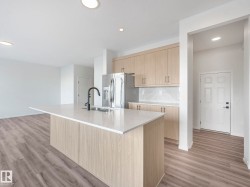 Kitchen with light wood finish cabinetry, a center island with sink, light stone counters, stainless steel refrigerator with ice dispenser, and light wood-style floors - 