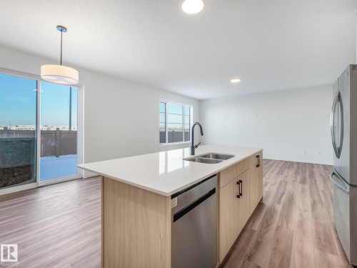 Kitchen featuring light wood finish cabinets, stainless steel appliances, pendant lighting, light wood-type flooring, and light stone countertops - 20506 16A Avenue, Edmonton, AB - Indoor Photo Showing Kitchen With Double Sink