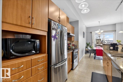 Kitchen featuring stainless steel appliances, light tile patterned flooring, a textured ceiling, light stone countertops, and hanging lights - 105 9707 105 Street, Edmonton, AB - Indoor Photo Showing Kitchen With Stainless Steel Kitchen With Double Sink With Upgraded Kitchen