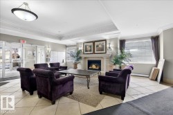 Living area featuring crown molding, light tile patterned floors, baseboard heating, a raised ceiling, and a warm lit fireplace - 