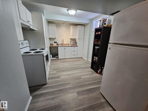 Kitchen featuring white appliances, white cabinetry, light wood-type flooring, and light countertops - 8512 131 Avenue, Edmonton, AB - Indoor Photo Showing Laundry Room