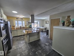 Kitchen with stainless steel appliances, island range hood, a kitchen island with sink, dark stone counters, and stone tile floors - 