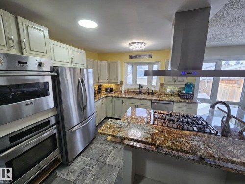 Kitchen featuring dark stone countertops, island exhaust hood, stainless steel appliances, tasteful backsplash, and dark stone finish floors - 8512 131 Avenue, Edmonton, AB - Indoor Photo Showing Kitchen With Upgraded Kitchen