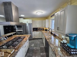 Kitchen with island range hood, black appliances, and light stone counters - 