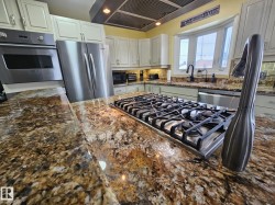 Kitchen featuring dark stone countertops, stainless steel appliances, extractor fan, backsplash, and white cabinets - 
