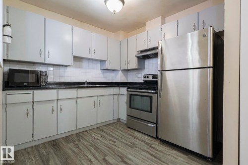 Kitchen featuring stainless steel appliances, dark countertops, tasteful backsplash, light wood-style floors, and white cabinets - 1526 69 Street Nw, Edmonton, AB - Indoor Photo Showing Kitchen