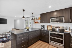Kitchen featuring stainless steel appliances, a peninsula, dark countertops, hanging light fixtures, and dark wood finish cabinets - 
