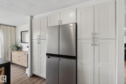 Kitchen with stainless steel appliances, a textured ceiling, light wood-type flooring, and white cabinets - 