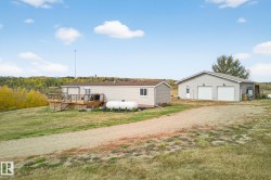 Manufactured / mobile home with a deck, an outdoor structure, a detached garage, driveway, and a front lawn - 