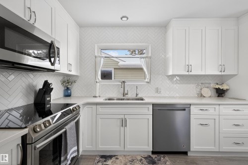 Kitchen with stainless steel appliances, white cabinets, light stone counters, and tasteful backsplash - 7719 71 Avenue, Edmonton, AB - Indoor Photo Showing Kitchen With Upgraded Kitchen