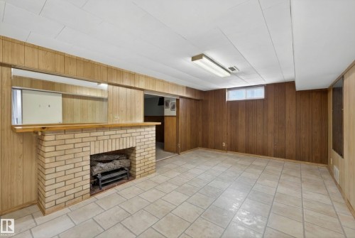 Basement featuring wood walls, a fireplace, and light tile patterned floors - 7719 71 Avenue, Edmonton, AB - Indoor With Fireplace
