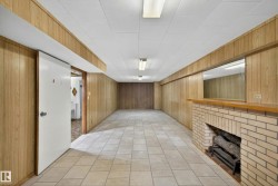 Finished below grade area featuring a brick fireplace, wood walls, and light tile patterned floors - 