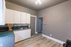 Kitchen with white cabinets, light wood-type flooring, dark countertops, and backsplash - 