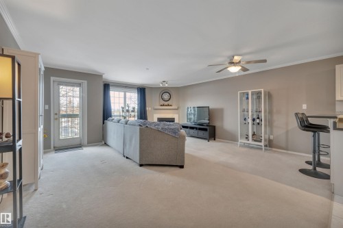 Living room with crown molding, light carpet, a ceiling fan, and a fireplace - 203 35 Sir Winston Churchill Avenue, St. Albert, AB - Indoor