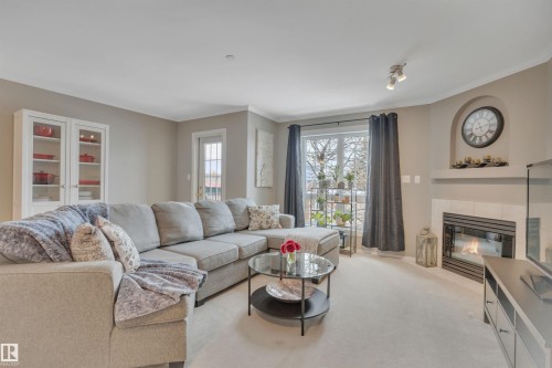 Carpeted living area featuring a tile fireplace and ornamental molding - 203 35 Sir Winston Churchill Avenue, St. Albert, AB - Indoor Photo Showing Living Room With Fireplace