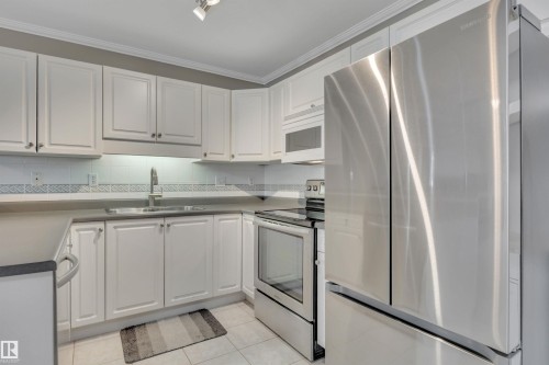 Kitchen with stainless steel appliances, white cabinets, light tile patterned floors, ornamental molding, and decorative backsplash - 203 35 Sir Winston Churchill Avenue, St. Albert, AB - Indoor Photo Showing Kitchen