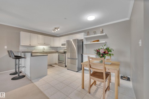 Kitchen with stainless steel appliances, a kitchen breakfast bar, white cabinets, a peninsula, and ornamental molding - 203 35 Sir Winston Churchill Avenue, St. Albert, AB - Indoor Photo Showing Kitchen