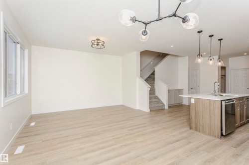 Kitchen with pendant lighting, an island with sink, light wood finished floors, and stainless steel dishwasher - 5111 Kinney Way Sw, Edmonton, AB - Indoor Photo Showing Kitchen