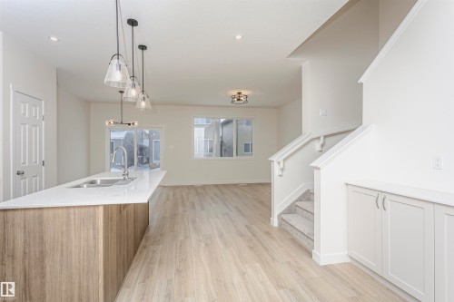 Kitchen featuring pendant lighting, light stone counters, light wood finished floors, and a kitchen island with sink - 5111 Kinney Way Sw, Edmonton, AB - Indoor Photo Showing Kitchen With Double Sink