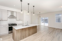 Two tone kitchen with stainless steel gas range oven, light wood-style floors, hanging light fixtures, tasteful backsplash, and dual tone cabinets - 