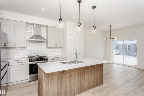Kitchen with stainless steel range with gas cooktop, light wood finished floors, a center island with sink, pendant lighting, and two tone cabinetry - 5111 Kinney Way Sw, Edmonton, AB - Indoor Photo Showing Kitchen With Double Sink With Upgraded Kitchen