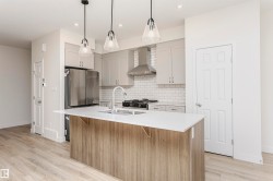 Kitchen featuring an island with sink, a breakfast bar area, pendant lighting, freestanding refrigerator, and light wood-type flooring - 