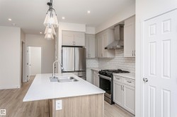 Kitchen with stainless steel appliances, light stone counters, decorative light fixtures, light wood finished floors, and a center island with sink - 