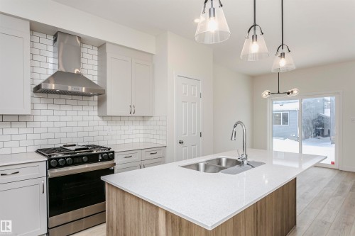 Dual tone kitchen featuring stainless steel gas range oven, light stone counters, decorative light fixtures, decorative backsplash, and light wood-style flooring - 5111 Kinney Way Sw, Edmonton, AB - Indoor Photo Showing Kitchen With Double Sink With Upgraded Kitchen