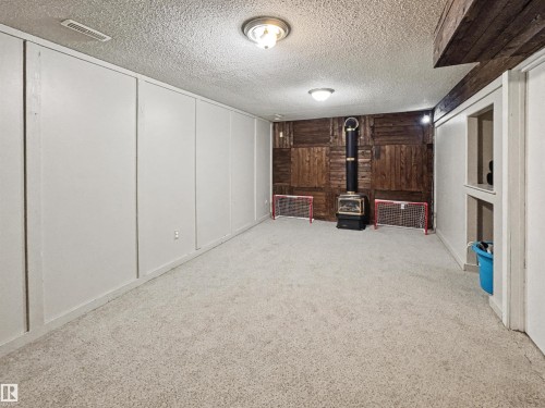 Finished below grade area featuring light colored carpet, a decorative wall, a textured ceiling, and a wood stove - 4602 42 Avenue, Bonnyville Town, AB - Indoor Photo Showing Other Room