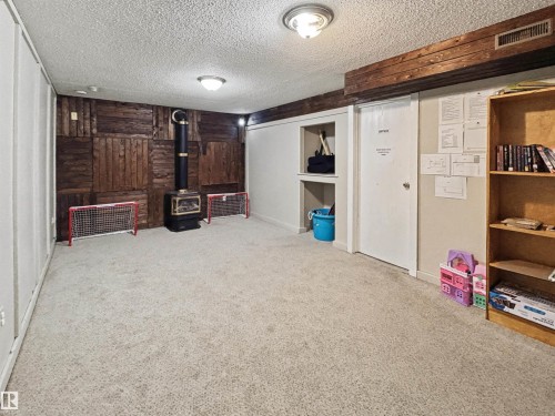Finished below grade area with wooden walls, light carpet, a textured ceiling, and a wood stove - 4602 42 Avenue, Bonnyville Town, AB - Indoor