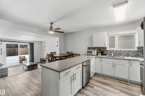 Kitchen featuring ceiling fan, white cabinets, light wood-style flooring, a peninsula, and tasteful backsplash - 11615 150 Avenue, Edmonton, AB - Indoor Photo Showing Kitchen
