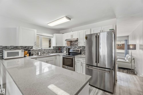 Kitchen with stainless steel appliances, light stone counters, white cabinetry, and light wood-type flooring - 11615 150 Avenue, Edmonton, AB - Indoor Photo Showing Kitchen With Upgraded Kitchen