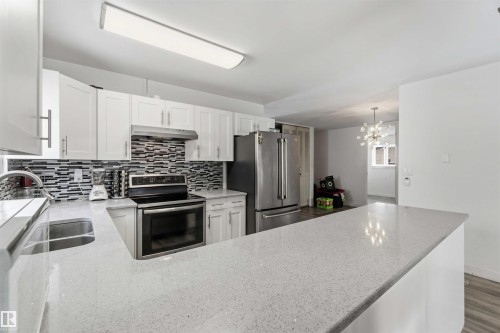 Kitchen with stainless steel appliances, light stone counters, white cabinetry, decorative backsplash, and hanging lights - 11615 150 Avenue, Edmonton, AB - Indoor Photo Showing Kitchen With Double Sink With Upgraded Kitchen