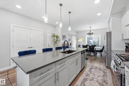 Kitchen with white cabinets, pendant lighting, light stone counters, a breakfast bar, and a center island with sink - 7803 Yorke Road, Edmonton, AB - Indoor Photo Showing Kitchen With Double Sink With Upgraded Kitchen